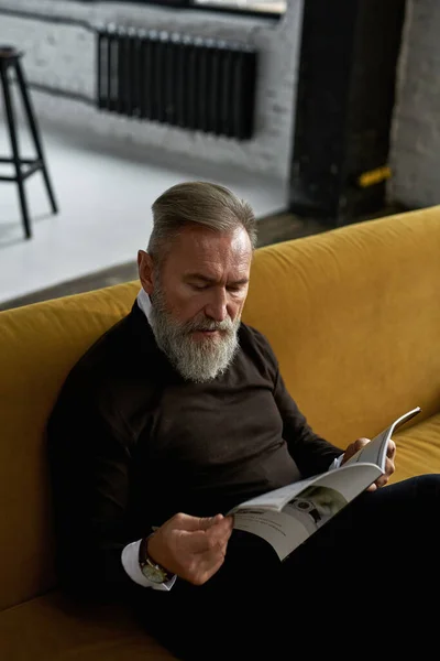 Elderly Concentrated Caucasian Man Reading Journal Sofa Spacious Apartment Trendy — Stock Photo, Image