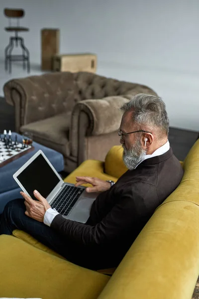 Elderly Caucasian Man Typing Laptop Sofa Spacious Apartment Trendy Bearded — Stock Photo, Image