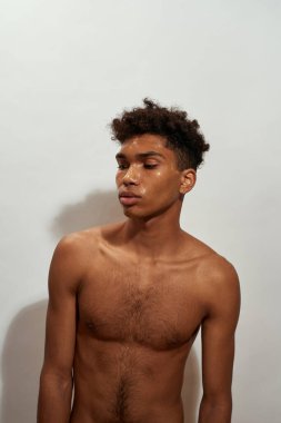 Focused black guy posing with golden mask on his face. Young slim brunette curly man with naked torso. Concept of facial skin care. Isolated on white background. Studio shoot. Copy space