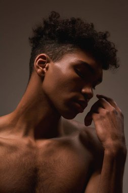 Cropped image of black handsome guy with closed eyes posing. Young brunette curly man with naked torso. Concept of modern male beauty. Isolated on brown background. Studio shoot