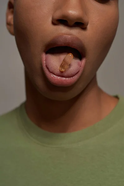 Close up of obscure face black guy with pill in his open mouth. Cropped man wearing t-shirt. Concept of modern young male lifestyle. Isolated on grey background. Studio shoot