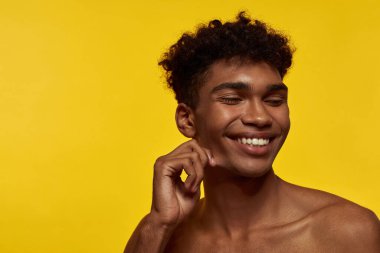 Partial image of smiling black good-looking guy with closed eyes. Young brunette curly model man. Concept of modern male beauty. Isolated on yellow background. Studio shoot. Copy space