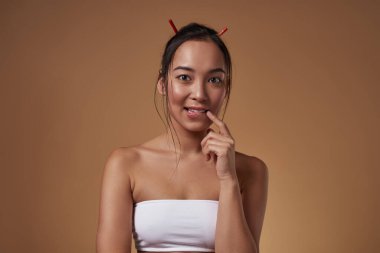 Utangaç Asyalı kız dudağını ısırıyor ve kameraya bakıyor. Kolsuz bluz giyen çekici, genç, esmer, zayıf kadın. Kadın güzelliği. Turuncu arka planda izole edilmiş. Stüdyo çekimi. Boşluğu kopyala