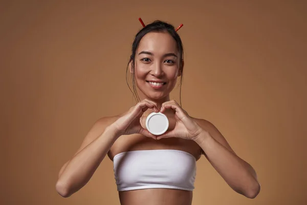 Smiling Fashionable Asian Girl Showing Container Cosmetic Cream Heart Gesture — Stockfoto