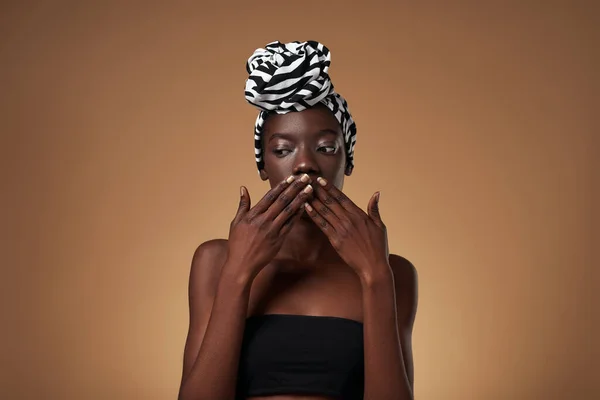 Confused Stylish Black Girl Wearing Traditional African Turban Covering Mouth — Stockfoto