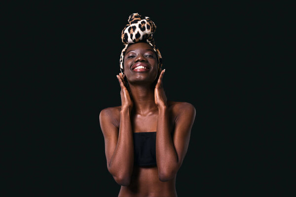 Front view of smiling black girl wearing traditional african turban posing and looking at camera. Pretty young slim woman wearing tank top. Female beauty. Black background. Studio shoot. Copy space