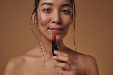 Cropped image of smiling elegant asian girl with lipstick looking at camera. Beautiful young brunette slim woman. Female beauty. Isolated on orange background. Studio shoot. Copy space