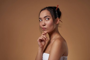 Side view of fashionable asian girl thinking about something. Pretty young brunette slim woman wearing tank top. Female beauty. Isolated on orange background. Studio shoot. Copy space