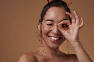 Partial of smiling elegant asian girl looking through binocular gesture. Beautiful young brunette slim woman. Female beauty. Isolated on orange background. Studio shoot. Copy space