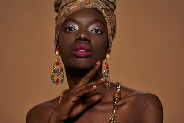 Partial of fashionable black girl wearing traditional african outfit and accessories looking at camera. Pretty young slim woman. Isolated on orange background. Studio shoot. Copy space