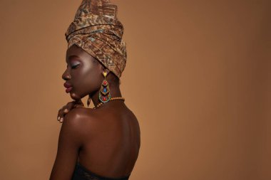 Side view of pensive fashionable black girl with closed eyes wearing traditional african outfit and accessories. Pretty young slim woman. Isolated on orange background. Studio shoot. Copy space