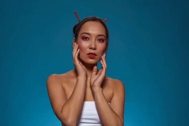 Portrait of confident elegant asian girl looking at camera. Beautiful young brunette slim woman wearing tank top. Female beauty. Isolated on blue background. Studio shoot. Copy space