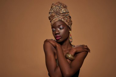 Partial of fashionable black girl wearing traditional african outfit and accessories thinking about something. Pretty young slim woman. Isolated on orange background. Studio shoot. Copy space