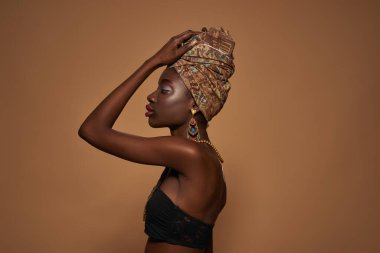 Side view of elegant black girl wearing traditional african outfit and accessories posing. Profile of beautiful young slim woman. Isolated on orange background. Studio shoot. Copy space