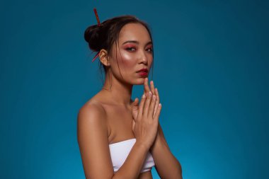 Partial of serious stylish chinese girl looking at camera. Attractive young brunette slim woman wearing tank top. Female beauty. Isolated on blue background. Studio shoot. Copy space