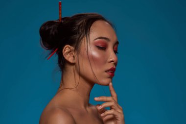 Cropped side view of thoughtful fashionable chinese or japanese girl. Pretty young brunette slim woman. Female beauty. Isolated on blue background. Studio shoot. Copy space