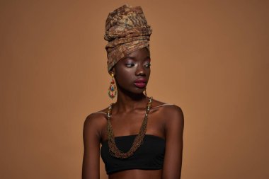 Focused stylish black girl wearing traditional african outfit and accessories looking away. Attractive young slim woman. Isolated on orange background. Studio shoot. Copy space
