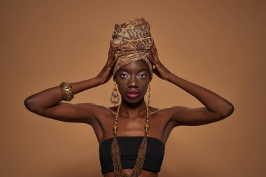 Front view of confident elegant black girl wearing traditional african outfit and accessories looking at camera. Beautiful young slim woman. Isolated on orange background. Studio shoot. Copy space