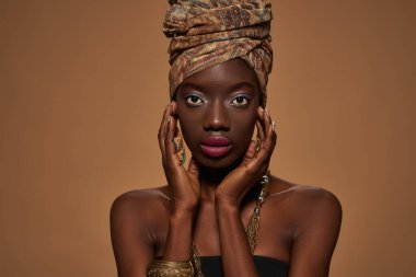 Cropped of confident stylish black girl wearing traditional african outfit and accessories looking at camera. Attractive young slim woman. Isolated on orange background. Studio shoot. Copy space