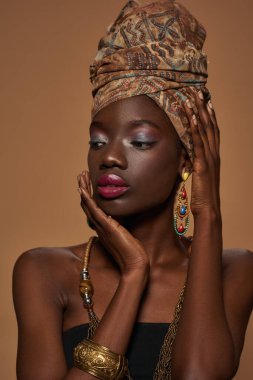 Cropped of stylish black girl wearing traditional african outfit and accessories. Attractive young slim woman wearing tank top, turban, necklace, earrings and bracelet. Orange background. Studio shoot