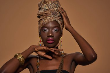 Confident fashionable black girl wearing traditional african outfit and accessories posing and looking at camera. Pretty young slim woman. Isolated on orange background. Studio shoot. Copy space