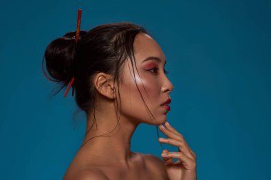 Partial side view of thoughtful stylish asian girl looking away. Profile of attractive young brunette slim woman. Female beauty. Isolated on blue background. Studio shoot. Copy space