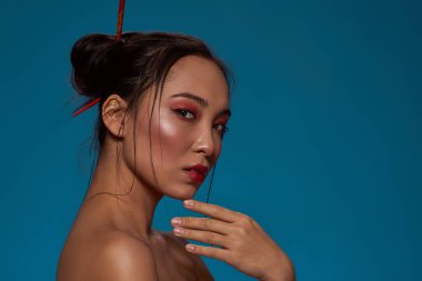 Cropped side view of confident elegant korean or chinese girl looking at camera. Beautiful young brunette slim woman. Female beauty. Isolated on blue background. Studio shoot. Copy space