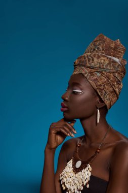 Profile off fashionable black girl thinking about something. Pretty young woman wearing traditional african outfit and accessories. Female beauty. Isolated on blue background. Studio shoot. Copy space