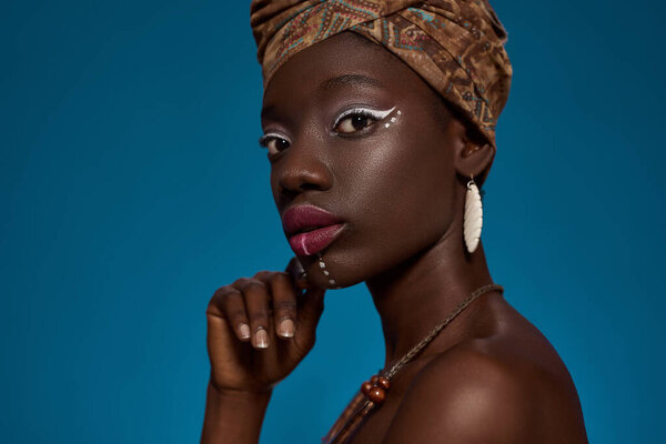 Cropped of elegant black girl looking at camera. Beautiful young slim woman wearing traditional african outfit and accessories. Female beauty. Isolated on blue background. Studio shoot. Copy space