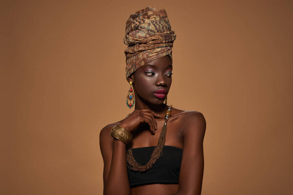 Concentrated fashionable black girl wearing traditional african outfit and accessories looking away. Pretty young slim woman. Isolated on orange background. Studio shoot. Copy space