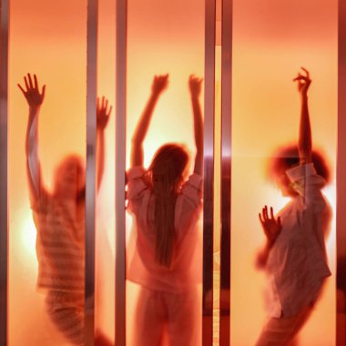 Orange silhouette of three girls dancing behind window of brick house during girlish sleepover at night. Girlfriends having fun and enjoying time together. Friendship. Rest, entertainment and leisure