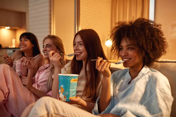Young Laughing Multiethnic Girlfriends Eating Ice Cream Watching Movie Sofa — Stockfoto
