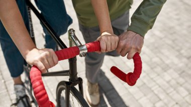 Partial of guy teaching his girlfriend riding bicycle in city. Modern urban teenager lifestyle. Entertainment, leisure and hobby. Biking. Teen relationship. Couple resting and spending time together