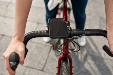 Selective focus of bicycle with smartphone riding cropped blurred girl on city pavement. Mobile phone for routing and geolocation. Modern urban healthy female lifestyle. Entertainment, leisure. Biking