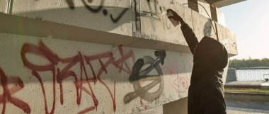 African american man drawing graffiti letters and symbols with aerosol can on concrete building in city. Street art. Hip hop culture. Guy wearing hoodie. Modern urban lifestyle. Sunny day