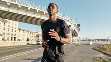 Young black sportsman running or jogging on city street. Handsome athletic slim guy wearing sportswear and looking away. Concept of modern healthy lifestyle. Warm sunny day