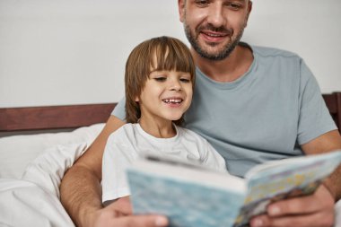 Baba ve küçük oğlu evde kitap okuyor. Genç, beyaz bir aile ilişkisi ve birlikte eğlenmek. Babalık ve ebeveynlik. Ev eğlencesi, hobi ve eğlence