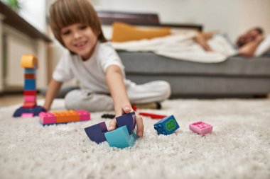 İnşaat taşlarının seçici odağı bulanık çocuğu evdeki kanepede babasının yanında yatırıyor. Genç, modern, beyaz aile yaşam tarzı ve ilişkisi. Ev eğlencesi, hobi ve eğlence