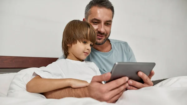 父と息子は自宅でデジタルタブレットを見ています 若い白人の家族関係 男の抱擁少年 父親と子育て 国内レジャー — ストック写真