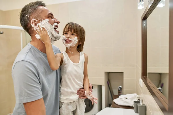 수염에 거품을 바르는 화장실에서 말이야 유쾌하게 감독하는 어린이와 사람은 농담을 — 스톡 사진