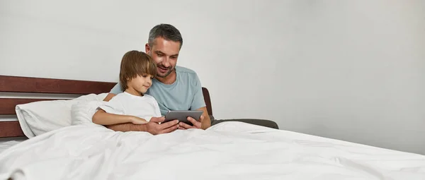 Pai Concentrado Filho Pequeno Assistindo Tablet Digital Cama Casa Relacionamento — Fotografia de Stock