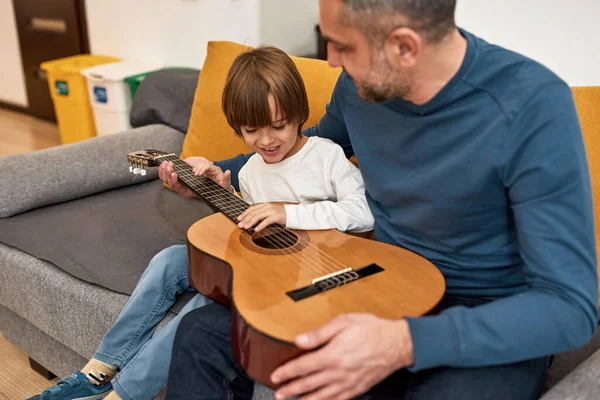 父は幼い息子に家庭でソファでアコースティックギターを弾いてノートを教えていた 白人の家族関係と一緒に時間を過ごす 父親と子育て 国内レジャー — ストック写真