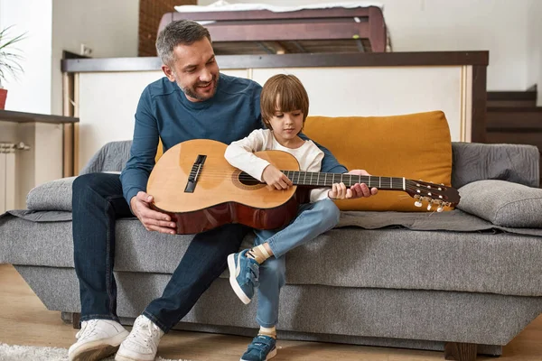 Pai Sorridente Ensinando Filho Tocar Guitarra Acústica Sofá Casa Relações — Fotografia de Stock