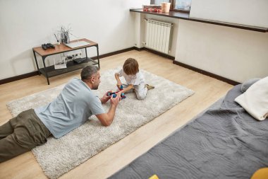 Baba ve küçük oğlu evdeki halıda inşaat taşlarıyla oynuyorlar. Genç beyaz bir aile birlikte vakit geçiriyor. Babalık ve ebeveynlik. Ev eğlencesi, hobi ve eğlence