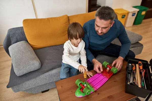 Visão Alto Ângulo Pai Olhando Para Pequeno Filho Fixando Skate — Fotografia de Stock