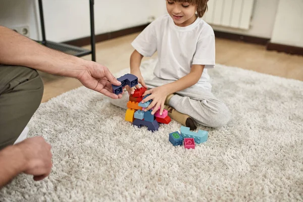 彼らが家でカーペットの上に設置された建設で遊んでいる間 作物の父は小さな息子に建物のブロックを与えます 家族関係だ 父親と子育て 国内レジャー — ストック写真