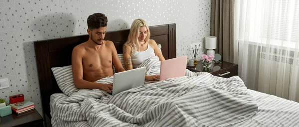 年轻而专注的多种族夫妇在家中使用笔记本电脑 白人女孩和中东男人休息 家庭娱乐和休闲 现代公寓的卧室 早上时间 — 图库照片