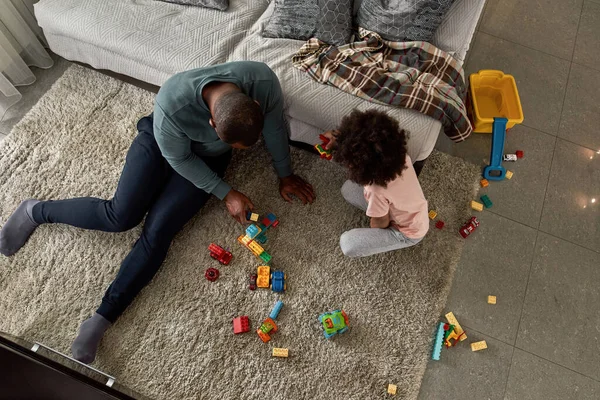 Top view of black father and son playing with construction building blocks on carpet at home. Man and child spending time together. Fatherhood and parenting. Domestic leisure, hobby and entertainment
