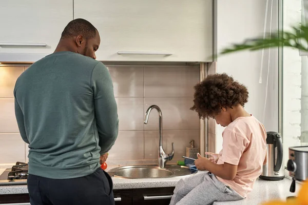 Homem Negro Cozinhando Salada Olhando Para Seu Filho Usando Tablet — Fotografia de Stock