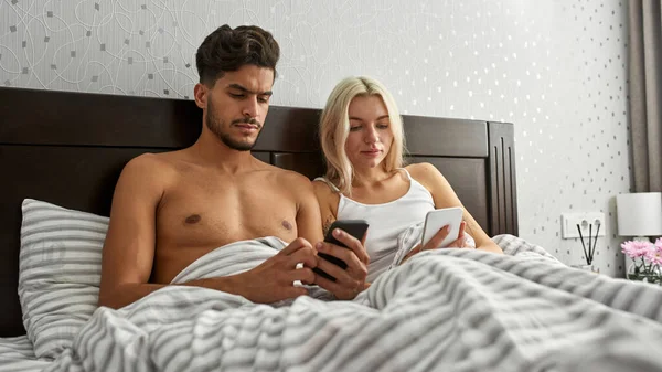 침대에서 스마트폰을 사용하는 커플에 초점을 맞추었다 여자와 남자가 쉬면서 시간을 — 스톡 사진